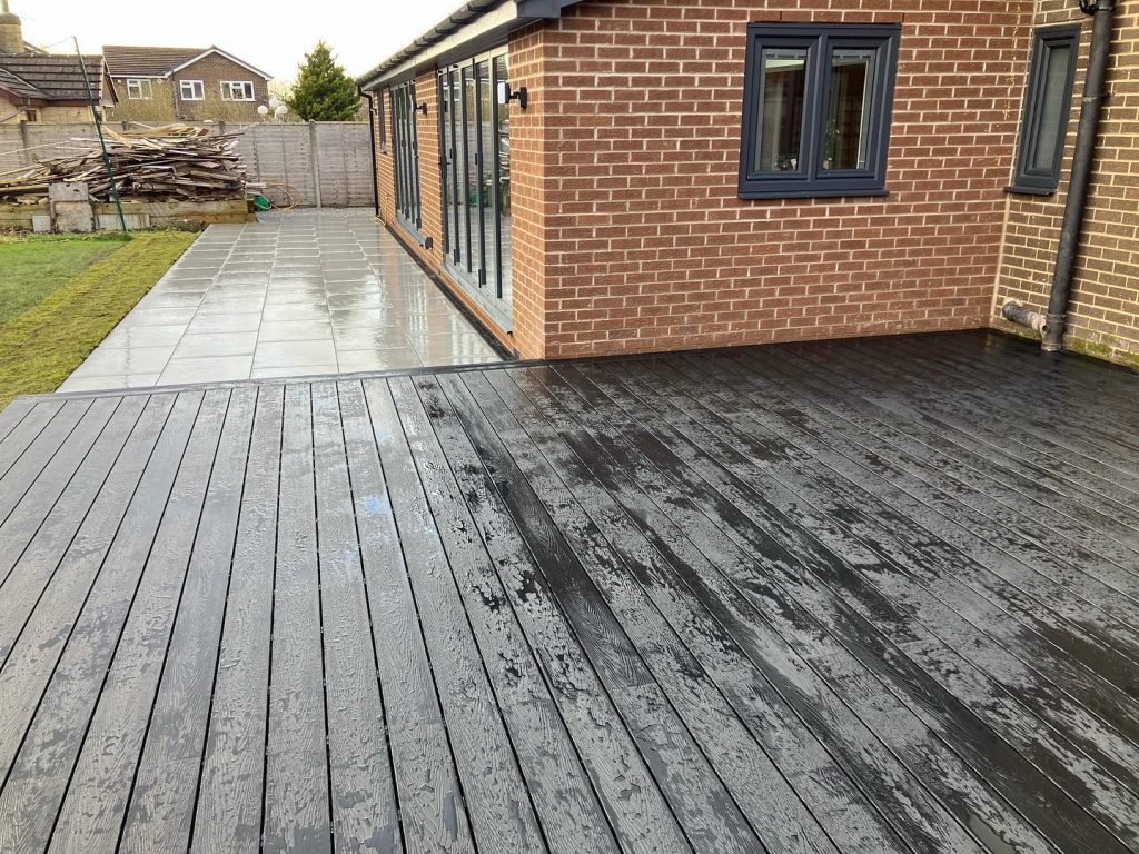 Large dark composite deck connecting a house to a newly paved garden